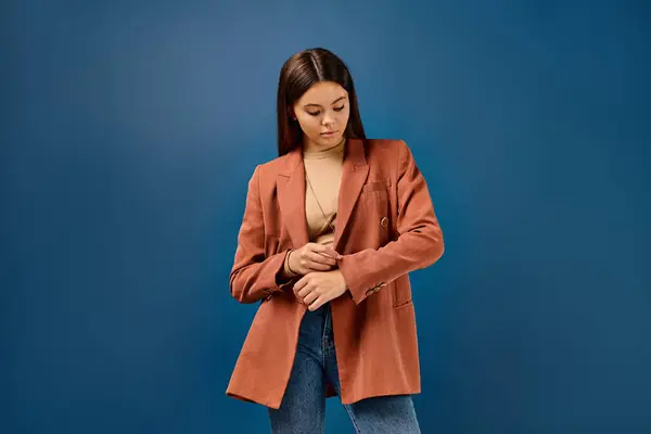 Pretty brunette stylish teenager with long hair in brown blazer posing on dark blue background — Stock Photo