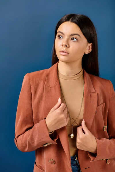 Adolescente de moda chica en elegante chaqueta marrón posando sobre fondo azul y mirando hacia otro lado - foto de stock