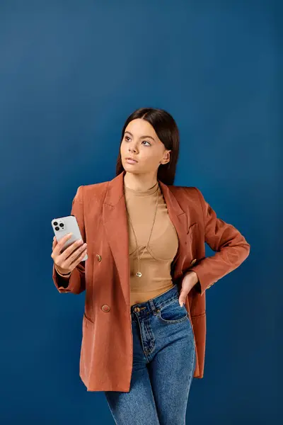 Очаровательная элегантная девушка-подросток в коричневом шикарном блейзере держит мобильный телефон и отворачивается — стоковое фото
