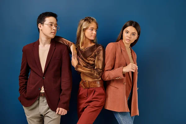 Fashionable interracial teenagers in elegant attires posing on blue backdrop, friendship day — Stock Photo