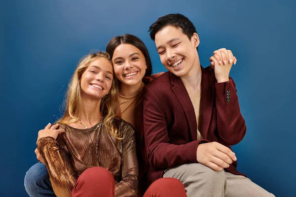 Joyful teenage girls smiling at camera next to their jolly elegant asian friend on blue background — Stock Photo