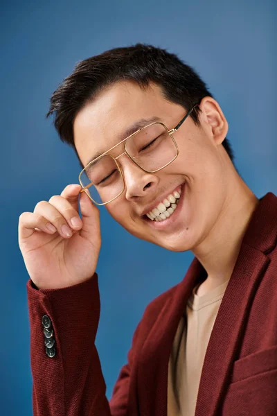 Joyeux asiatique élégant adolescent garçon avec lunettes dans élégant tenue regardant caméra sur fond bleu — Photo de stock