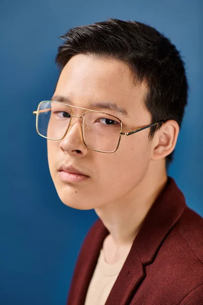 Good looking asian teenage boy with glasses in stylish attire looking at camera on blue backdrop — Stock Photo