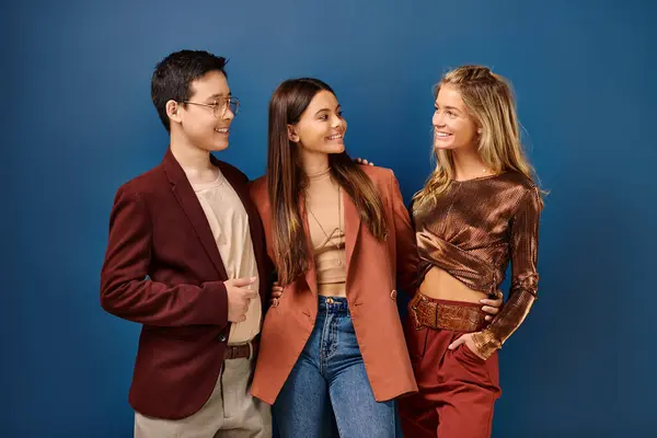 Adorable jolly diverse teens in stylish vibrant clothes having fun on blue backdrop, friendship day — Stock Photo