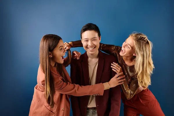 Jolly teenage girls in vivid attires having fun with their asian cheerful friend on blue backdrop — Stock Photo