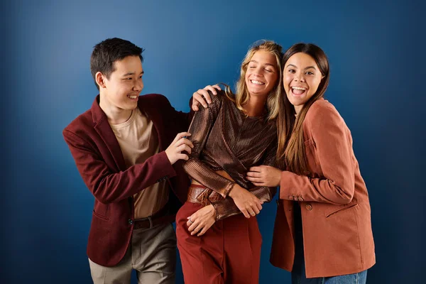 Jolly multiracial teenage friends in fashionable attires having fun together on blue backdrop — Stock Photo