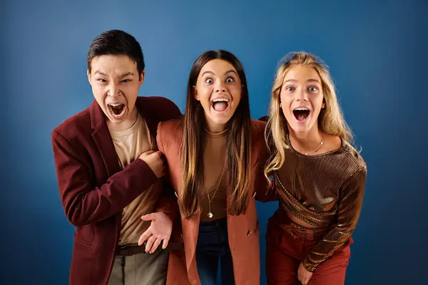 Jolly interracial adolescents in chic vivid attires posing together on blue backdrop, friendship day — Stock Photo