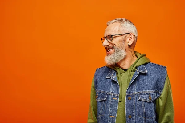 Joyous handsome mature man in vibrant hoodie and vest with glasses smiling and looking away — Stock Photo