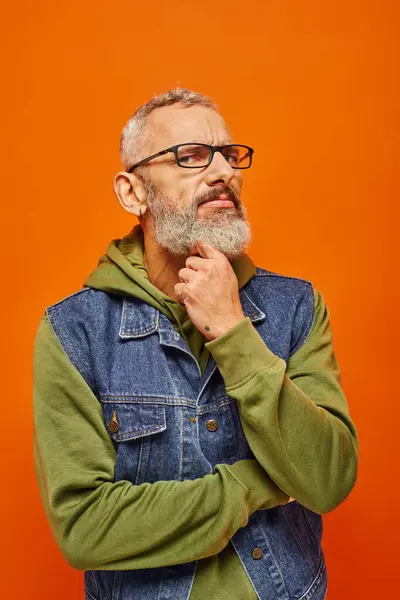 Homme mature concentré en sweat à capuche vert vibrant et gilet en denim posant et regardant la caméra — Photo de stock