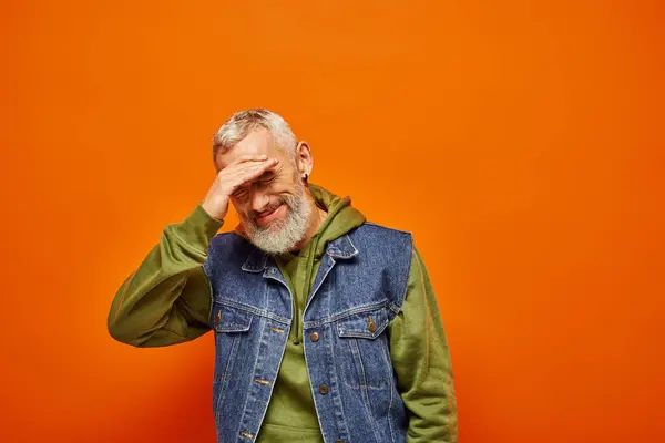 Joyeux beau mature homme en tenue vive avec barbe grise souriant à la caméra sur fond orange — Photo de stock