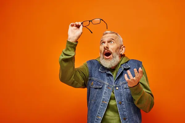 Gut aussehende überraschte reife Mann in lebendiger Kleidung mit Brille und posiert auf orangefarbenem Hintergrund — Stockfoto