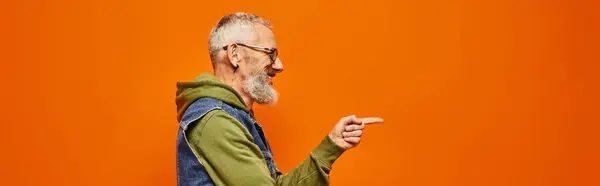 Bello gioioso uomo maturo in abito vibrante posa di profilo e indicando davanti a lui, banner — Foto stock