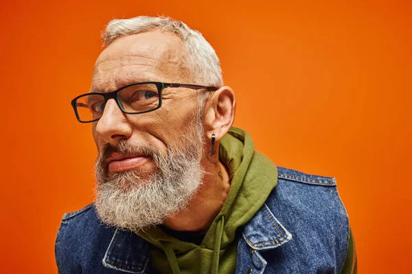 Fröhlich gut aussehende reife männliche Modell mit Brille posiert auf orangefarbenem Hintergrund und sucht ta Kamera — Stockfoto