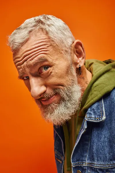 Bello allegro modello maschile con barba grigia in posa su sfondo arancione e sorridente alla macchina fotografica — Foto stock