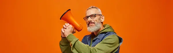 Funky joyeux homme mature avec barbe et lunettes posant avec mégaphone et regardant la caméra, bannière — Photo de stock