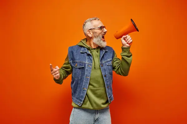 Good looking emotional mature male model in denim vest and stylish hoodie talking into megaphone — Stock Photo
