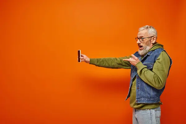 Good looking mature male model in vibrant clothes with beard and glasses holding smartphone — Stock Photo