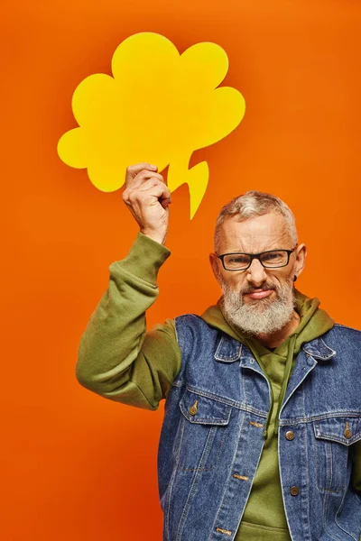Angry mature man in vibrant green hoodie posing with thought bubble above head and looking at camera — Stock Photo