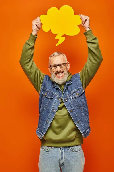 Jolly handsome mature man in vibrant attire holding thought bubble above head and smiling at camera — Stock Photo