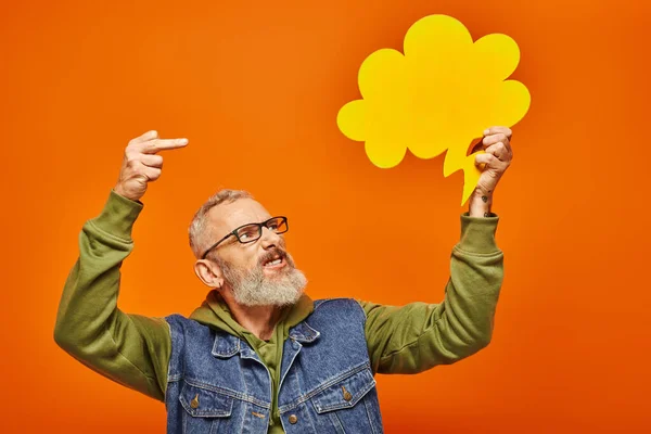 Bonne recherche bouleversé mature homme regardant bulle de pensée et montrant majeur doigt sur fond orange — Photo de stock