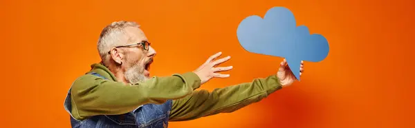 Surprised mature handsome man in vivid hoodie and stylish holding thought bubble in his hand, banner — Stock Photo