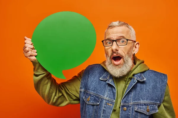 Shocked handsome mature male model in vibrant attire holding speech bubble and looking at camera — Stock Photo