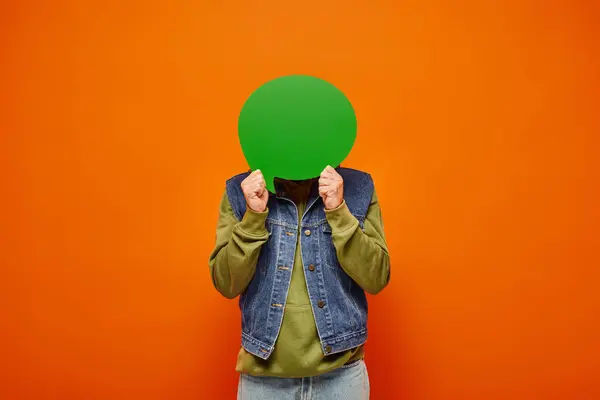 Modelo masculino maduro en ropa vibrante de moda sosteniendo burbuja de habla verde en frente de su cara - foto de stock