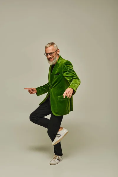 Bom olhar modelo masculino maduro em verde blazer vibrante de pé em uma perna e sorrindo alegremente — Fotografia de Stock