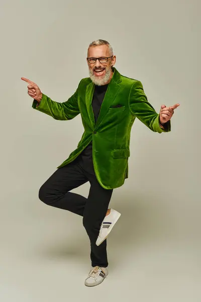 Guapo hombre maduro alegre en chaqueta verde vibrante posando en una pierna y sonriendo a la cámara - foto de stock