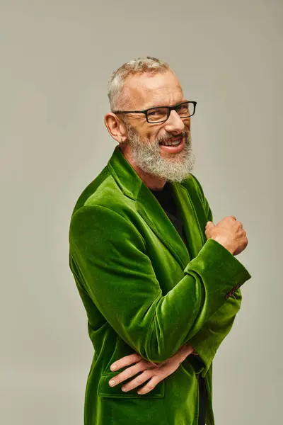 Alegre guapo maduro hombre en vibrante chaqueta verde con barba y gafas sonriendo a la cámara - foto de stock