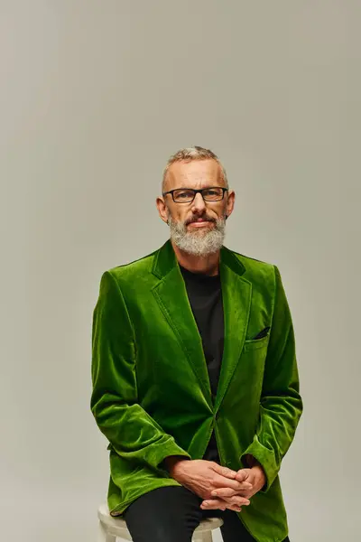 Attractive mature male model with glasses and gray beard in green blazer sitting on tall chair — Stock Photo