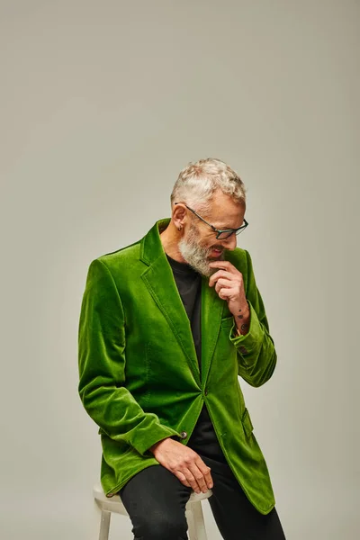 Guapo hombre maduro alegre en traje vibrante con gafas y barba sentado en una silla alta - foto de stock