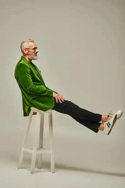 Schöne flippige ältere männliche Modell in heller Kleidung mit Accessoires posiert auf einem hohen Stuhl im Profil — Stockfoto
