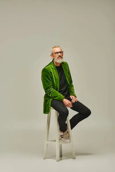 Good looking mature male model with beard and glasses sitting on tall chair and looking at camera — Stock Photo