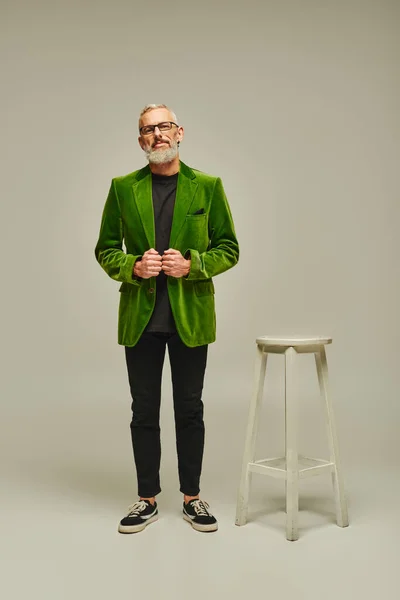 Красивый зрелый мужчина модель в стильном зеленом блейзере позирует рядом с высоким стулом и смотрит в камеру — стоковое фото