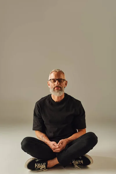 Attraktiver ruhiger, reifer Mann, der mit überkreuzten Beinen auf dem Boden sitzt und vor beigem Hintergrund meditiert — Stockfoto