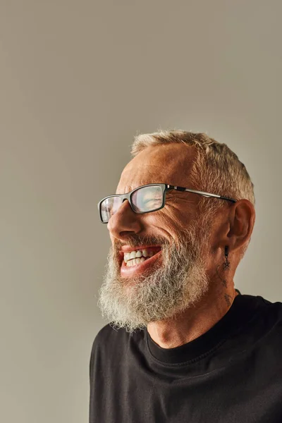 Portrait of jolly mature man with tattoo in black t shirt smiling happily on beige backdrop — Stock Photo