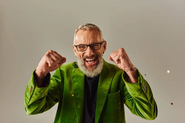 Cheerful handsome mature man in green blazer smiling and showing fists at camera on beige backdrop — Stock Photo