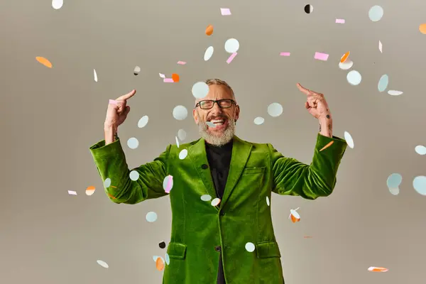 Cheeky jolly mature man with closed eyes in green blazer showing middle fingers under confetti rain — Stock Photo