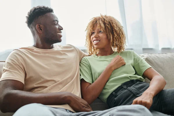 Felice donna africana americana in bretelle guardando fidanzato mentre seduto sul divano, tempo di qualità — Foto stock