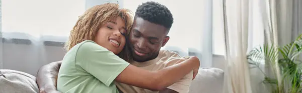 Happy african american woman in braces embracing boyfriend while sitting on couch, banner — Stock Photo