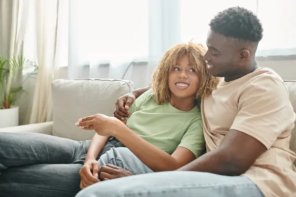 Black man embracing happy girlfriend in braces while sitting on cozy couch in living room — Stock Photo