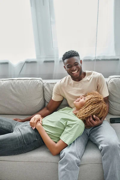 Glückliches afrikanisch-amerikanisches Paar lacht zusammen, während es sich auf dem Sofa im Wohnzimmer entspannt, Zweisamkeit — Stockfoto
