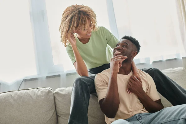 Freudige afrikanisch-amerikanische Frau schaut ihren Freund im Wohnzimmer an, schwarzes Paar und hochwertige Zeit — Stockfoto