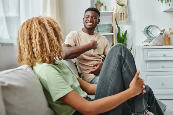 Glücklicher schwarzer Mann lächelt, während er seine Freundin im Wohnzimmer ansieht und Zeit mit Qualität verbringt — Stockfoto