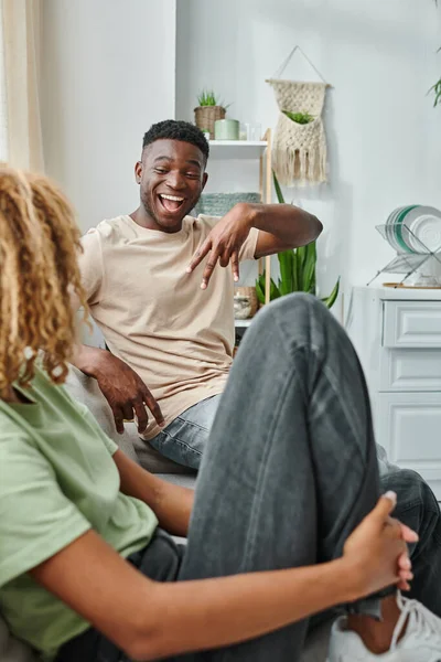Felice uomo nero sorridente mentre comunica con il linguaggio dei segni con la fidanzata in soggiorno — Foto stock