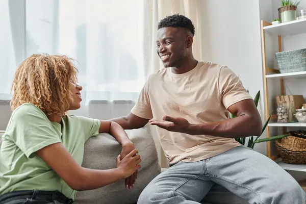 Heureux noir homme souriant tout en utilisant le langage des signes pour la communication avec petite amie dans les bretelles — Photo de stock