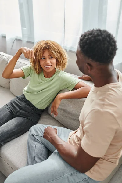 Щаслива чорна жінка в брекетах сидить на дивані і дивиться на хлопця, невербальне спілкування — стокове фото