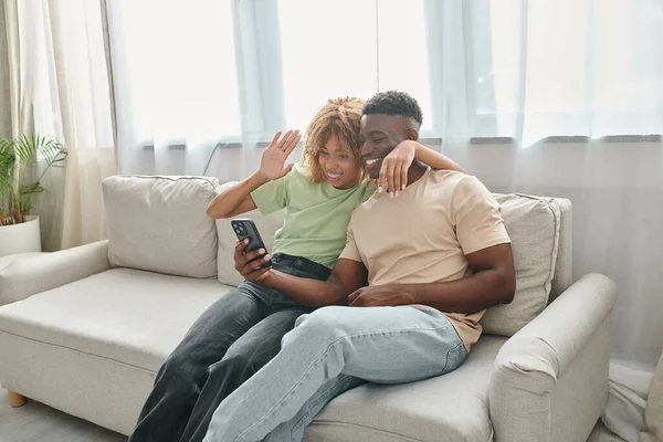 Feliz casal afro-americano vídeo conversando em um smartphone enquanto sentados no sofá juntos — Fotografia de Stock