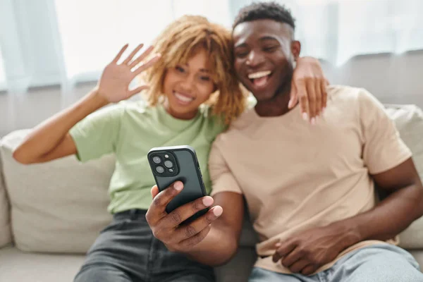 Foco no smartphone, feliz casal afro-americano vídeo bate-papo e acenando na sala de estar — Fotografia de Stock